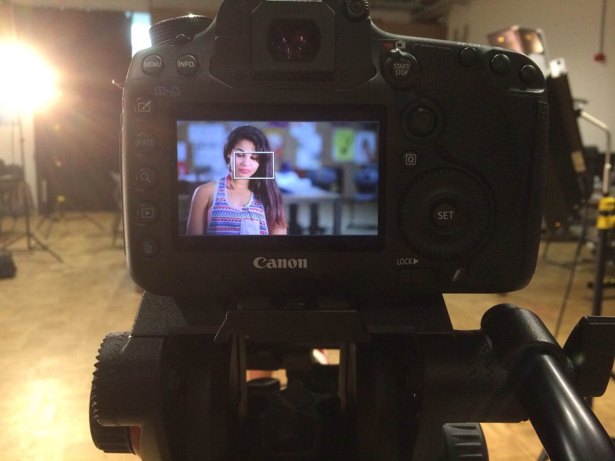 [IMAGE] The back of a video camera. On the screen is a seated, young woman with brown skin, looking down.