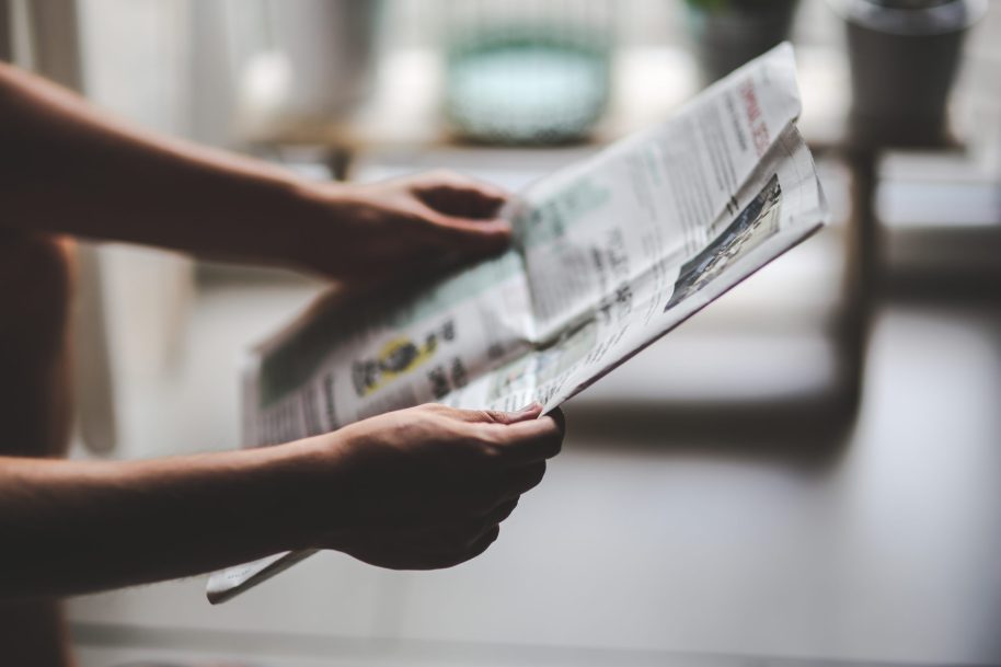 [IMAGE] A pair of white male hands holding a newspaper suggesting that someone out of shot is reading the newspaper