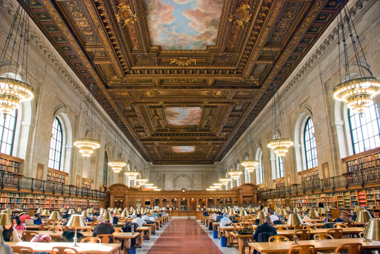 [IMAGE] The New York Public Library main branch reading room. People seated at large desks under a painted ceiling with window lined walls